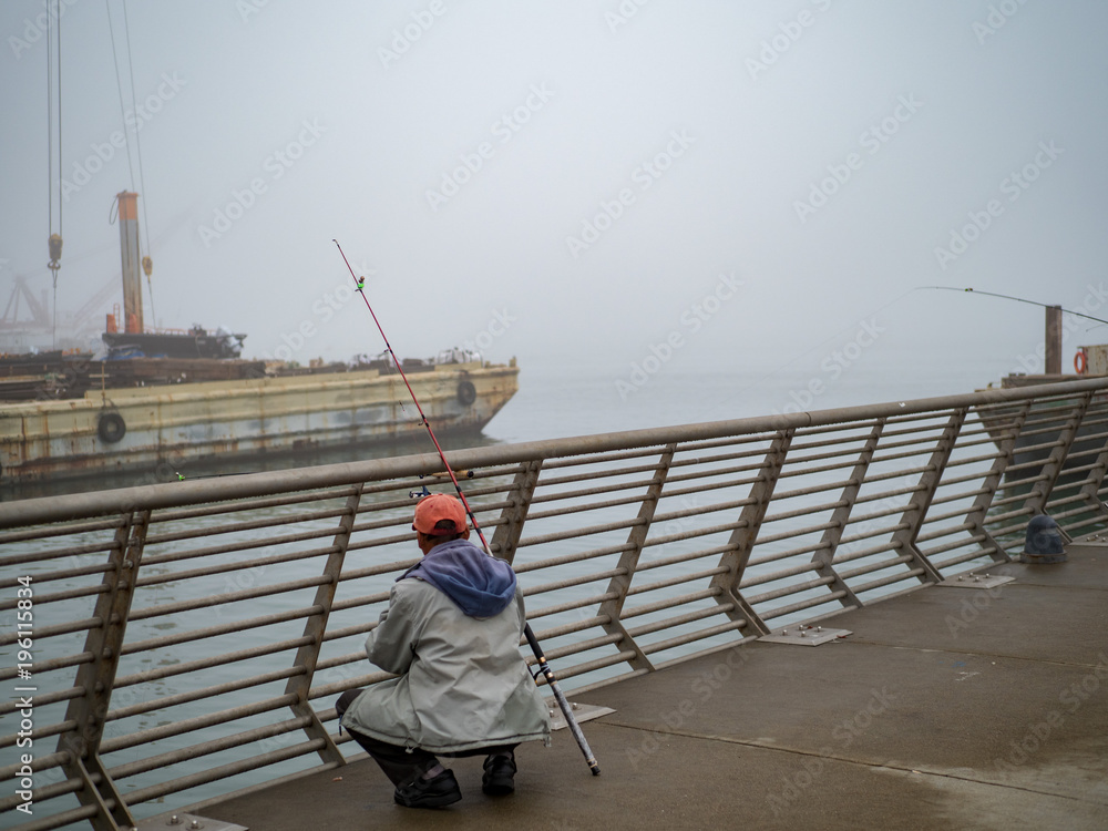 Fishermen examining catch on industrial pier on foggy day