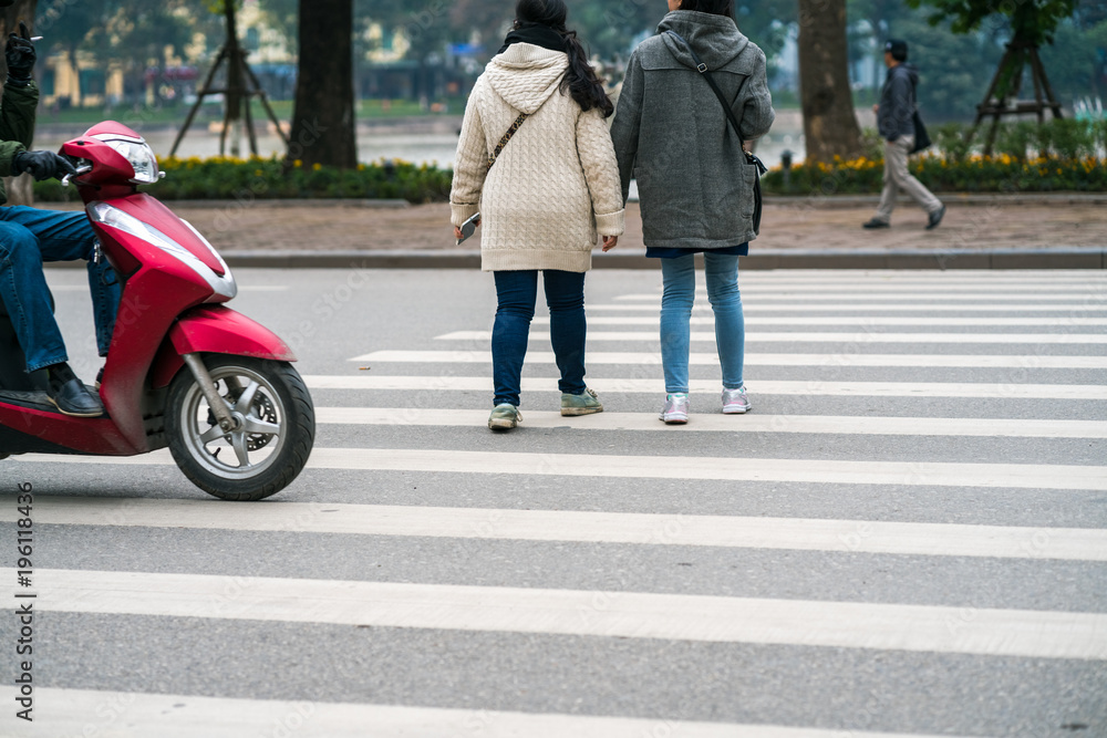 People walking across a street while motorbikes keep running on street in Hanoi, Vietnam. Closeup People walking across a street while motorbikes keep running on street in Hanoi, Vietnam. Closeup