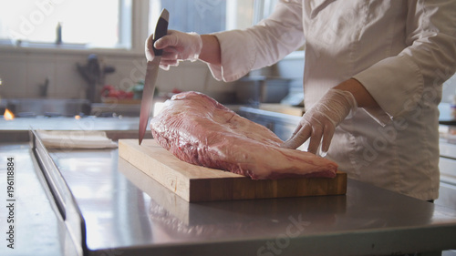 Butcher prepairs large piece of fresh raw meat lying on a wooden board in a commercial kitchen