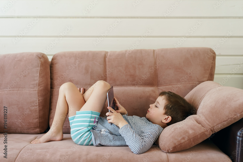 cute boy in casual clothes lying on the couch watching and playing tablet  in the house Stock Photo | Adobe Stock