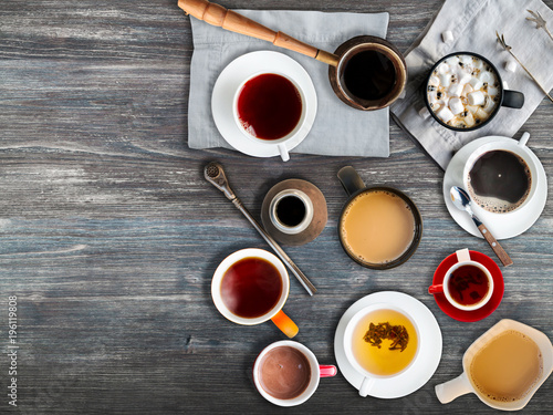 Set of different hot drinks in cups and mugs served on wooden table - tea bar, coffee shop, restaurant, warming drinks concept. Top view, copy space.