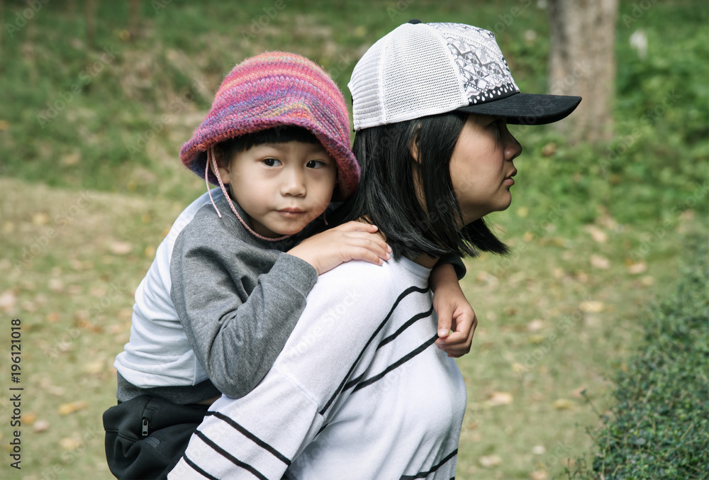 Young mother keeping her son on back outside