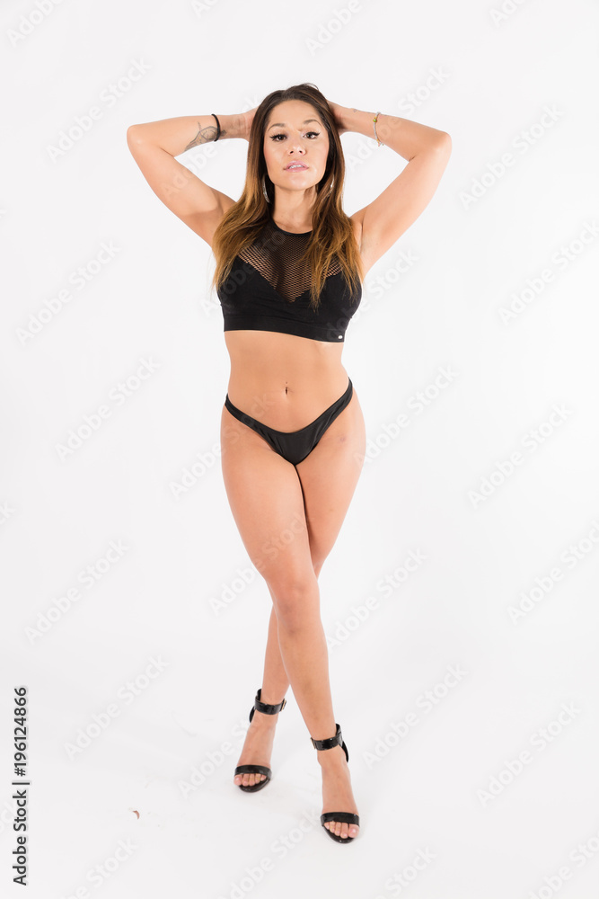 Young fit hispanic woman in black two piece and black high heels posing on a white background Young fit hispanic woman in black two piece and black high heels posing on a white background