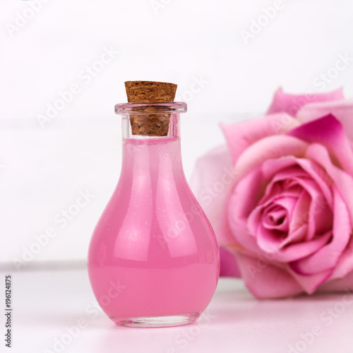 rose essential oil bottle blurred rose flower white background square