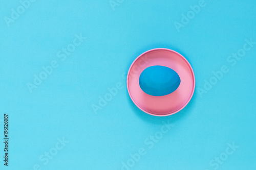 The blue Easter egg lies in a brightly pink metal box. Blue background. Copy space.