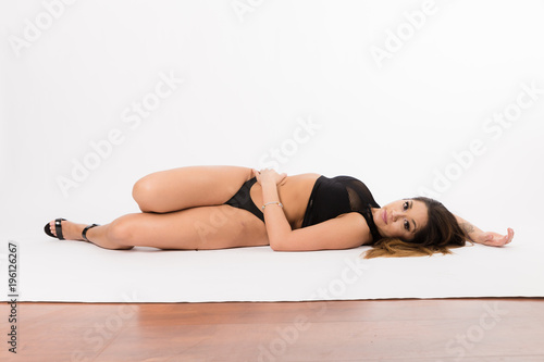 Young fit hispanic woman in black two piece and black high heels posing on a white background