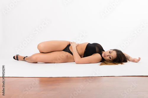 Young fit hispanic woman in black two piece and black high heels posing on a white background