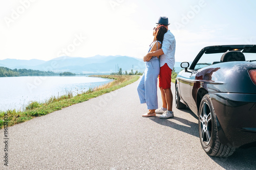 Couple in love stands near the cabriolet car on the picturesque mountain road