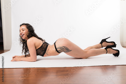 Young fit mixed race woman in black two piece and black high heels posing on a white background
