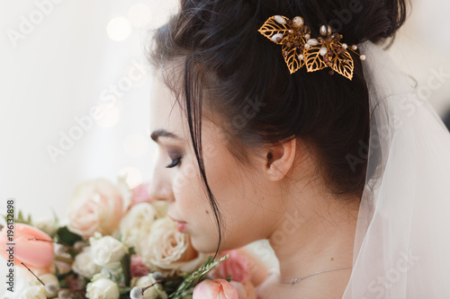 Back view of young brunette bride with barrette in hair. Flower bouquet on background. Close-up facial portrait