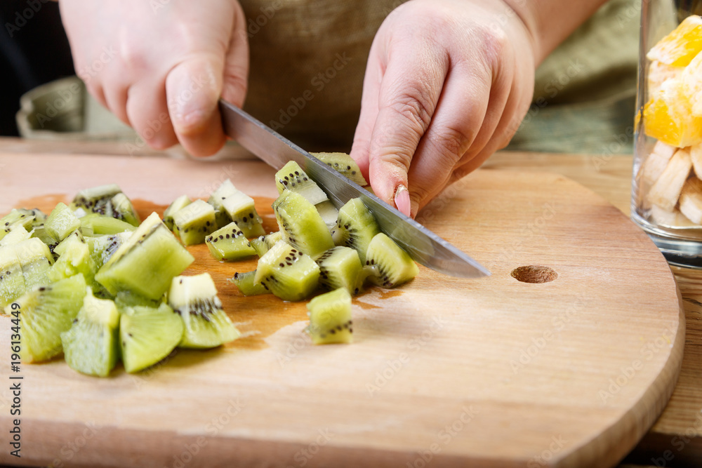 A woman cuts into small pieces of a kiwi knife on a wooden board. Close-up, horizontal frame A woman cuts into small pieces of a kiwi knife on a wooden board. Close-up, horizontal frame