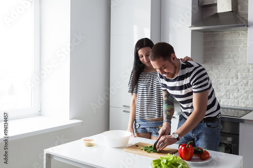 Smiling young couple cooking healthy food in the white home kitchen together