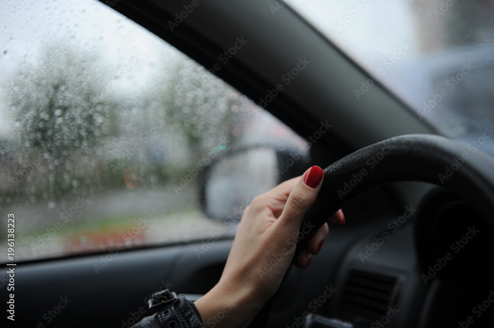 Woman with leather jacket holding hand on steering wheel on a rainy day