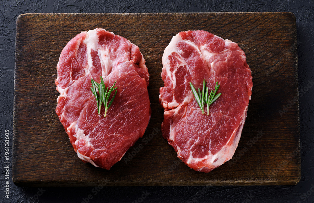 Fresh raw pork steaks and rosemary on a dark wooden background. Fresh raw pork steaks and rosemary on a dark wooden background.