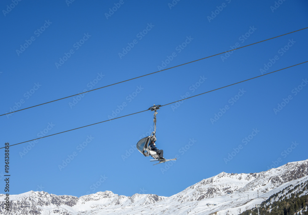 Two skiers man sitting on the a cable car and going to the top of mountain with blue sky background