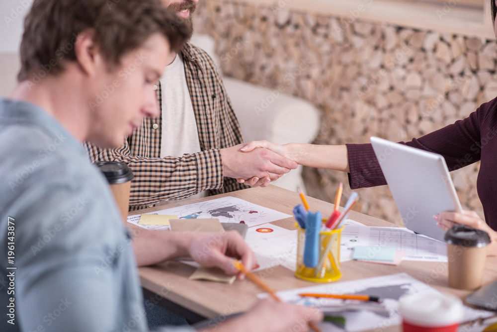 At work. Nice pleasant delighted people sitting at the table and shaking hands while meeting each other At work. Nice pleasant delighted people sitting at the table and shaking hands while meeting each other