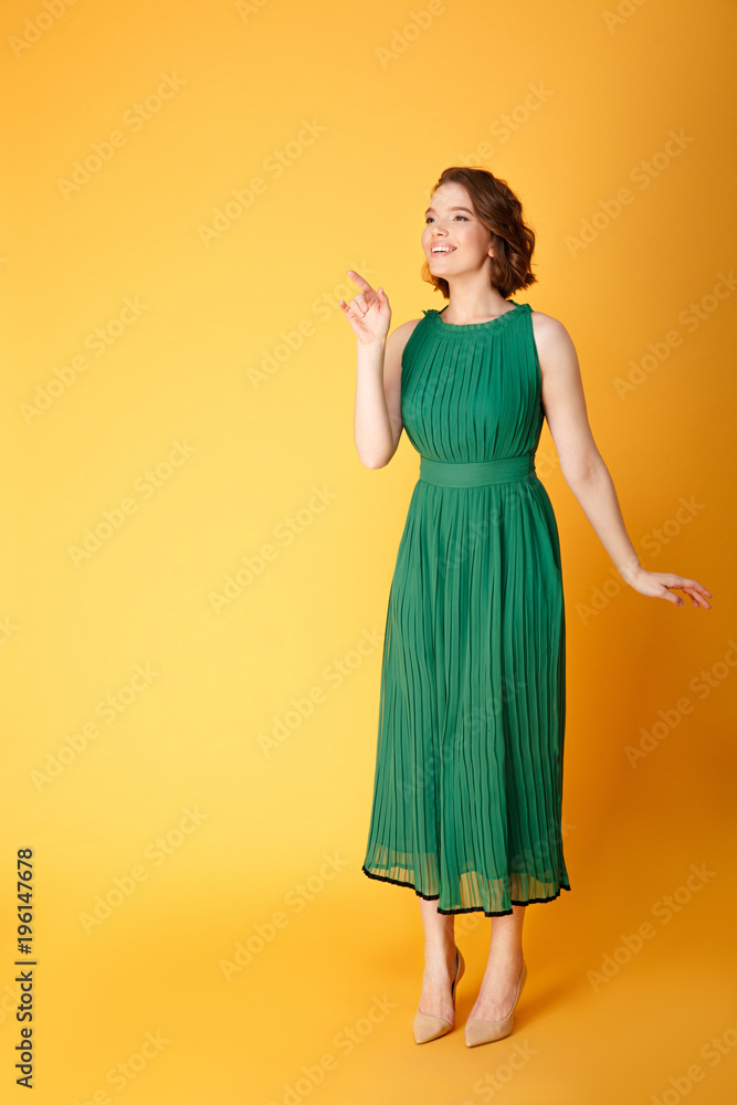 young smiling woman in green dress pointing away isolated on orange young smiling woman in green dress pointing away isolated on orange