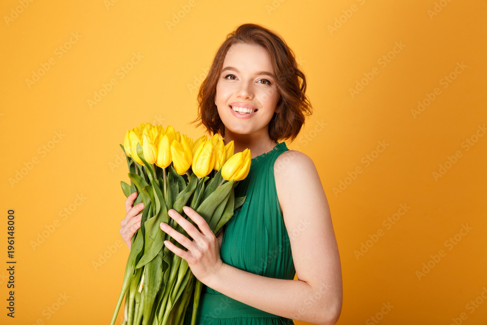 portrait of cheerful woman in green dress with bouquet of yellow tulips isolated on orange portrait of cheerful woman in green dress with bouquet of yellow tulips isolated on orange