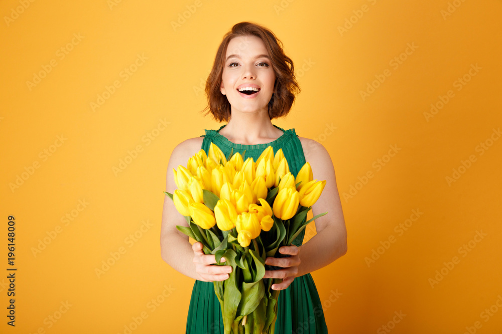 happy young woman holding bouquet of yellow tulips in hands isolated on orange happy young woman holding bouquet of yellow tulips in hands isolated on orange