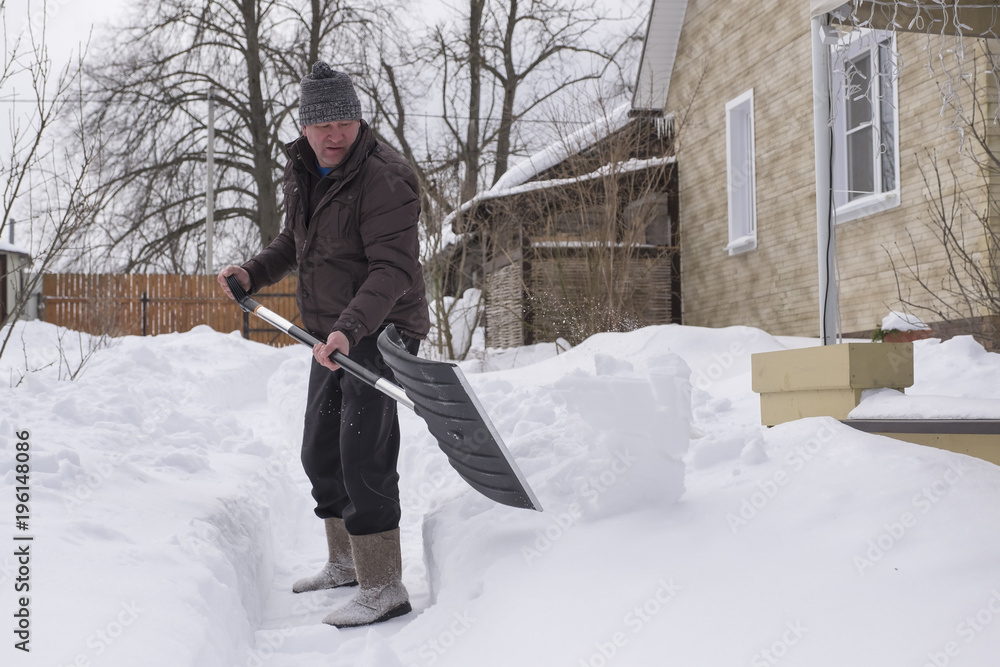 A man cleans a shovel of snow on a site in a country house after a snowstorm.
