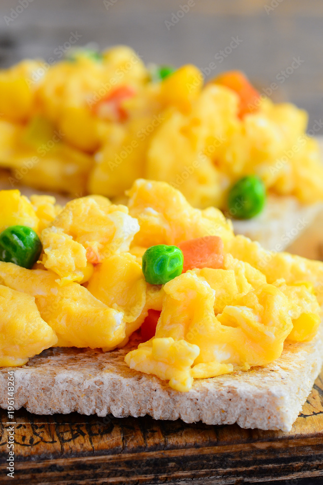 Delicious scrambled eggs with vegetables on crispy toast. Scrambled omelette toast recipe. Simple homemade cooking. Vertical photo. Closeup Delicious scrambled eggs with vegetables on crispy toast. Scrambled omelette toast recipe. Simple homemade cooking. Vertical photo. Closeup