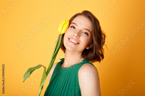 portrait of smiling woman with yellow tulip isolated on orange