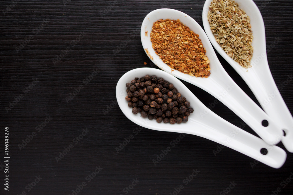 Black and red pepper, set of spices in spoons. On black wooden table Black and red pepper, set of spices in spoons. On black wooden table