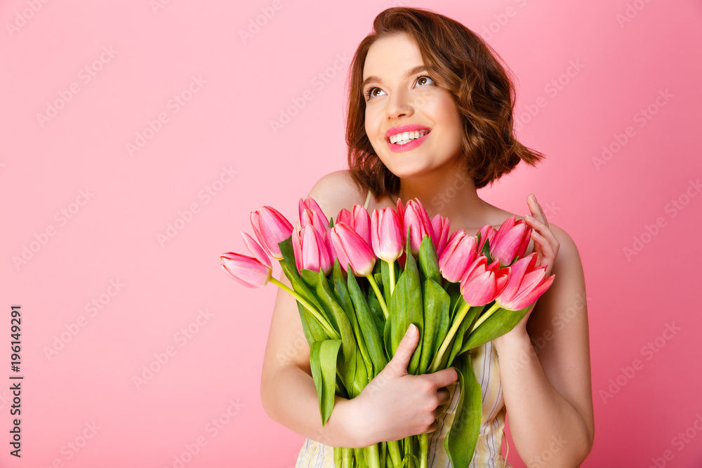 portrait of cheerful woman with bouquet of spring tulips isolated on pink