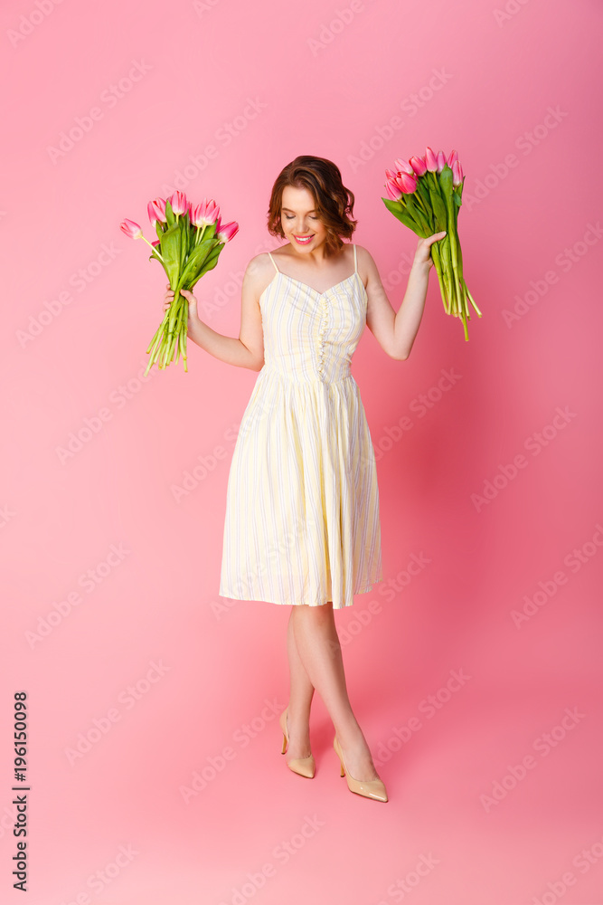 cheerful woman with bouquets of tulips isolated on pink