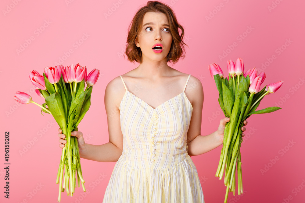 portrait of confused woman with bouquets of tulips isolated on pink