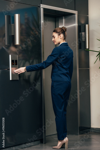 Young businesswoman pressing button of elevator