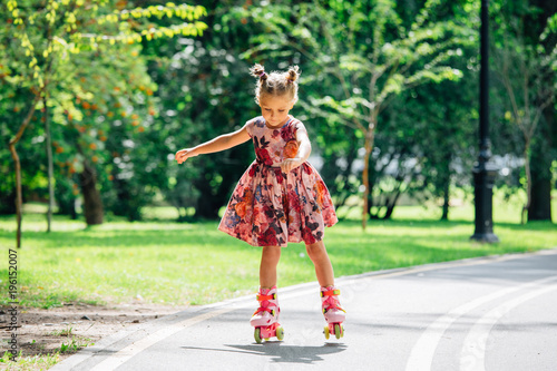Little pretty girl on roller skates in dress in park. Cheerful child having fun outdoors