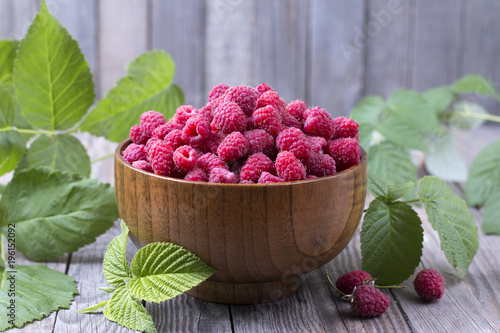 Red fresh raspberries on brown rustic wood background. Bowl with natural ripe organic berries with peduncles, green leaves photo