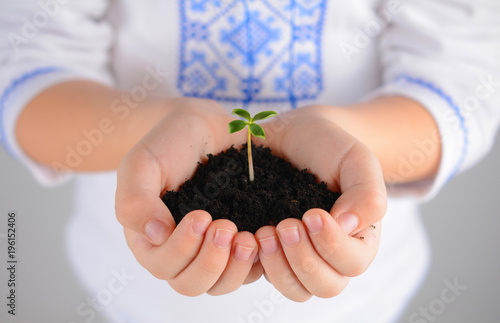 Child holding young plant with soil in hands as Earth Day conception.