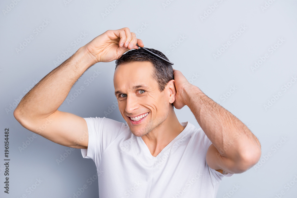 Neat, trendy, experienced, stylish, brunet, positive man looking at camera, combing, fixing, correcting his hair with hairbrush, holding hand on head, isolated on grey background Neat, trendy, experienced, stylish, brunet, positive man looking at camera, combing, fixing, correcting his hair with hairbrush, holding hand on head, isolated on grey background