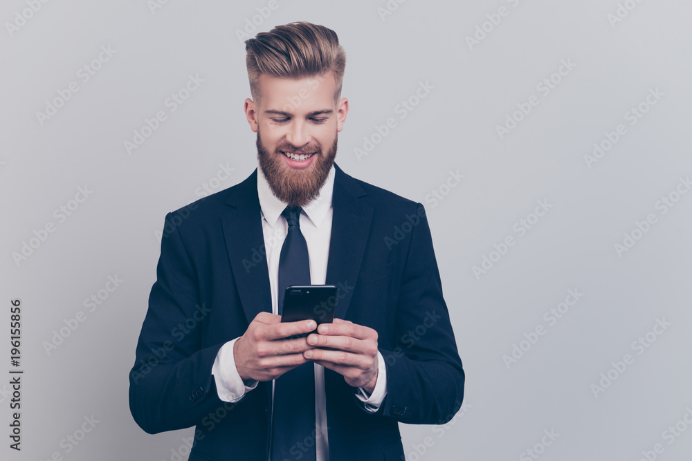 Portrait of handsome with stylish hairdo cheerful funny excited financier using smartphone playing online games receiving getting writing sms updating his digital gadget isolated on gray background Portrait of handsome with stylish hairdo cheerful funny excited financier using smartphone playing online games receiving getting writing sms updating his digital gadget isolated on gray background