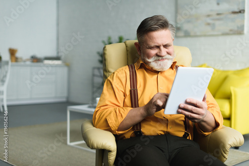 smiling bearded senior man using digital tablet at home