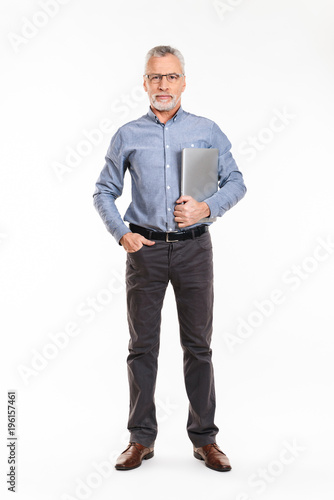 Confident mature man holding laptop and looking camera seriously