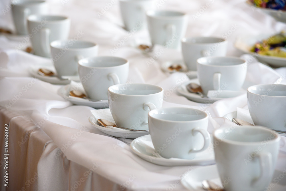 Many white coffee cups in a line over a buffet Many white coffee cups in a line over a buffet