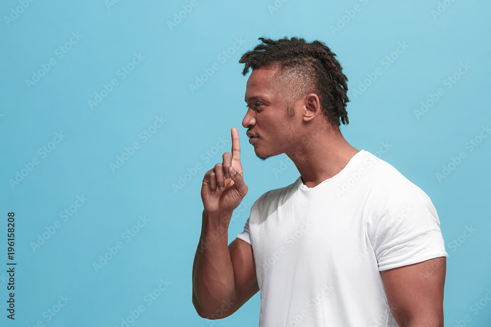 The young afro-american man whispering a secret behind her hand over blue background The young afro-american man whispering a secret behind her hand over blue background