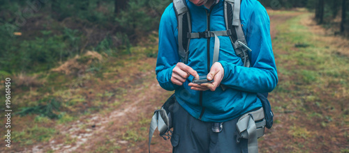 Young male backpacker with smartphone on forest path.