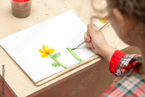 A girl draws a drawing with paints on a sheet