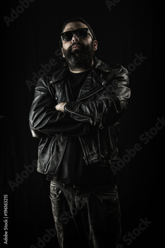 Tough guy in black leather jacket and sunglasses with arms crossed.