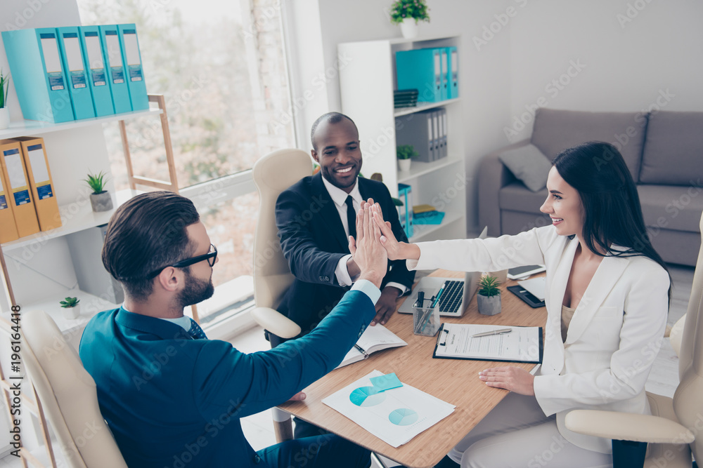 Obraz premium Power of friendship in business company. Three attractive happy smiling joyful smart professional confident elegant partners holding palms clasped together, sitting in workplace, workstation