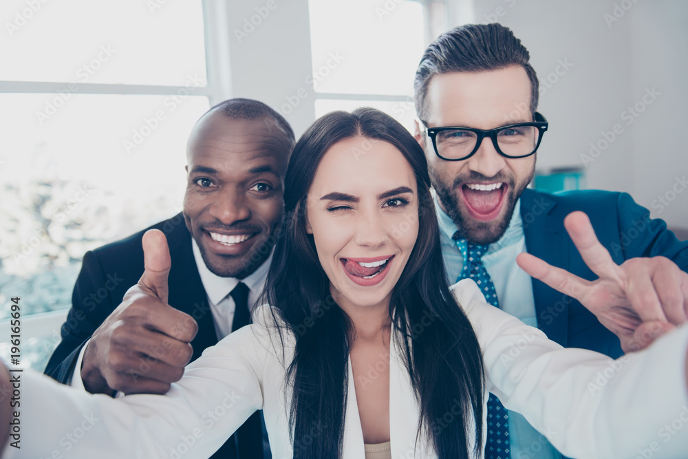 Three comic, funny, crazy partners, colleagues having fun, men with bristle showing like symbol and two fingers, peace sign with hands, girl shooting selfie and gesture tongue out, wink with one eye Three comic, funny, crazy partners, colleagues having fun, men with bristle showing like symbol and two fingers, peace sign with hands, girl shooting selfie and gesture tongue out, wink with one eye
