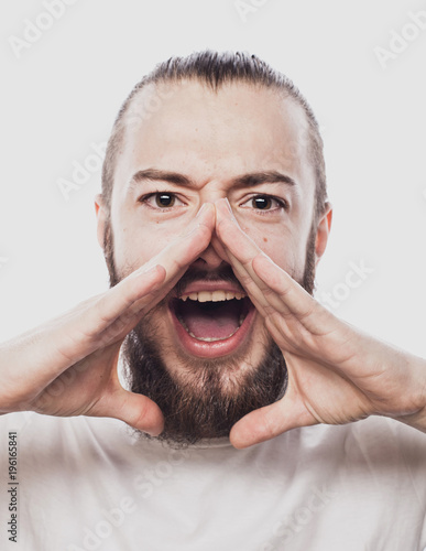 Scream and shout! Handsome young man holding hands near opened mouth. Isolated on white.