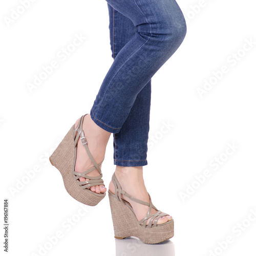 Female legs in jeans and gray sandals on a wedge