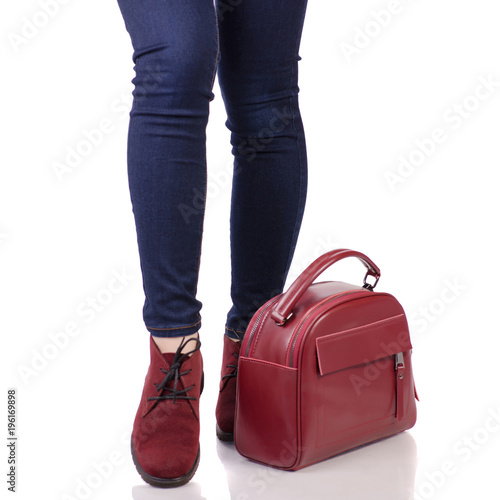 Female legs in jeans and in red suede shoes with red leather bag handbag