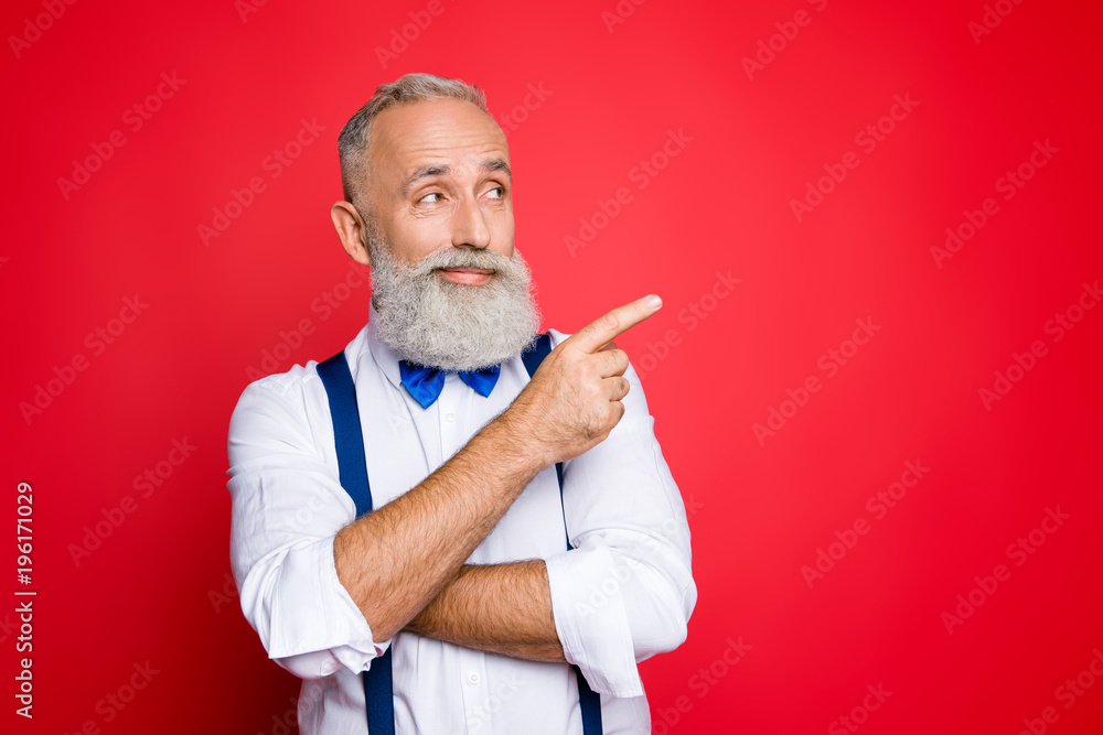 © deagreez - Portrait with copy space of minded, ponder, professional, retro stylist, barber with blue bowtie and suspenders pointing on empty place, product with forefinger, isolated on red background © deagreez - Portrait with copy space of minded, ponder, professional, retro stylist, barber with blue bowtie and suspenders pointing on empty place, product with forefinger, isolated on red background