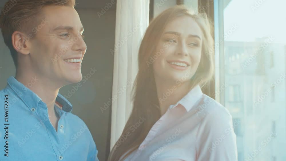Portrait of happy couple standing together near the window in their new apartment. Portrait of happy couple standing together near the window in their new apartment.